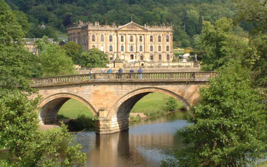 Large country house by river with wooded hillside beyond