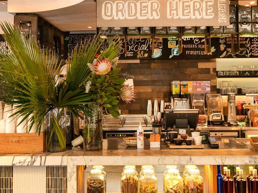 Front counter of The Botanical Cafe with fresh flowers, spice jars and stacked takeaway coffee cups.