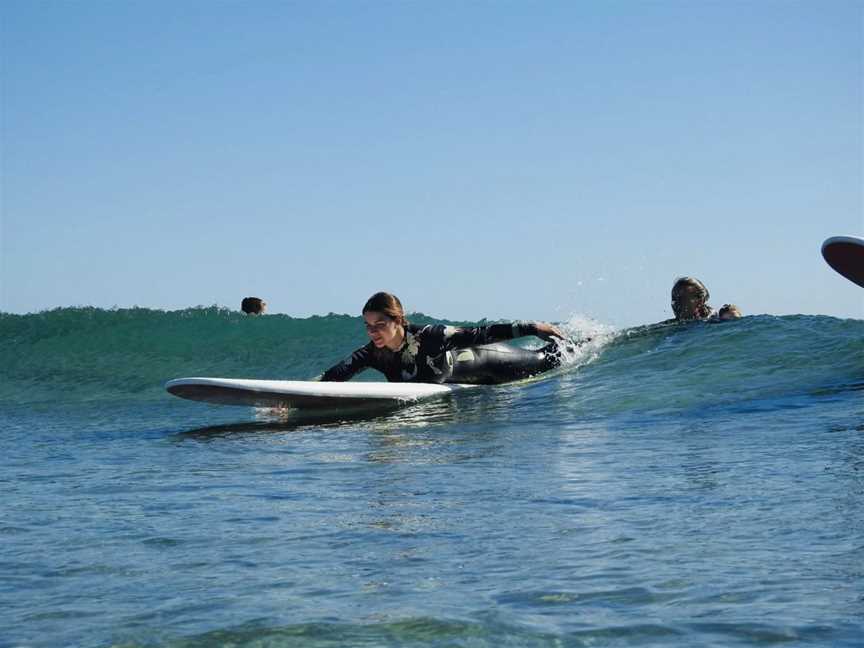 Student getting pushed into a green unbroken wave during a surf lesson.